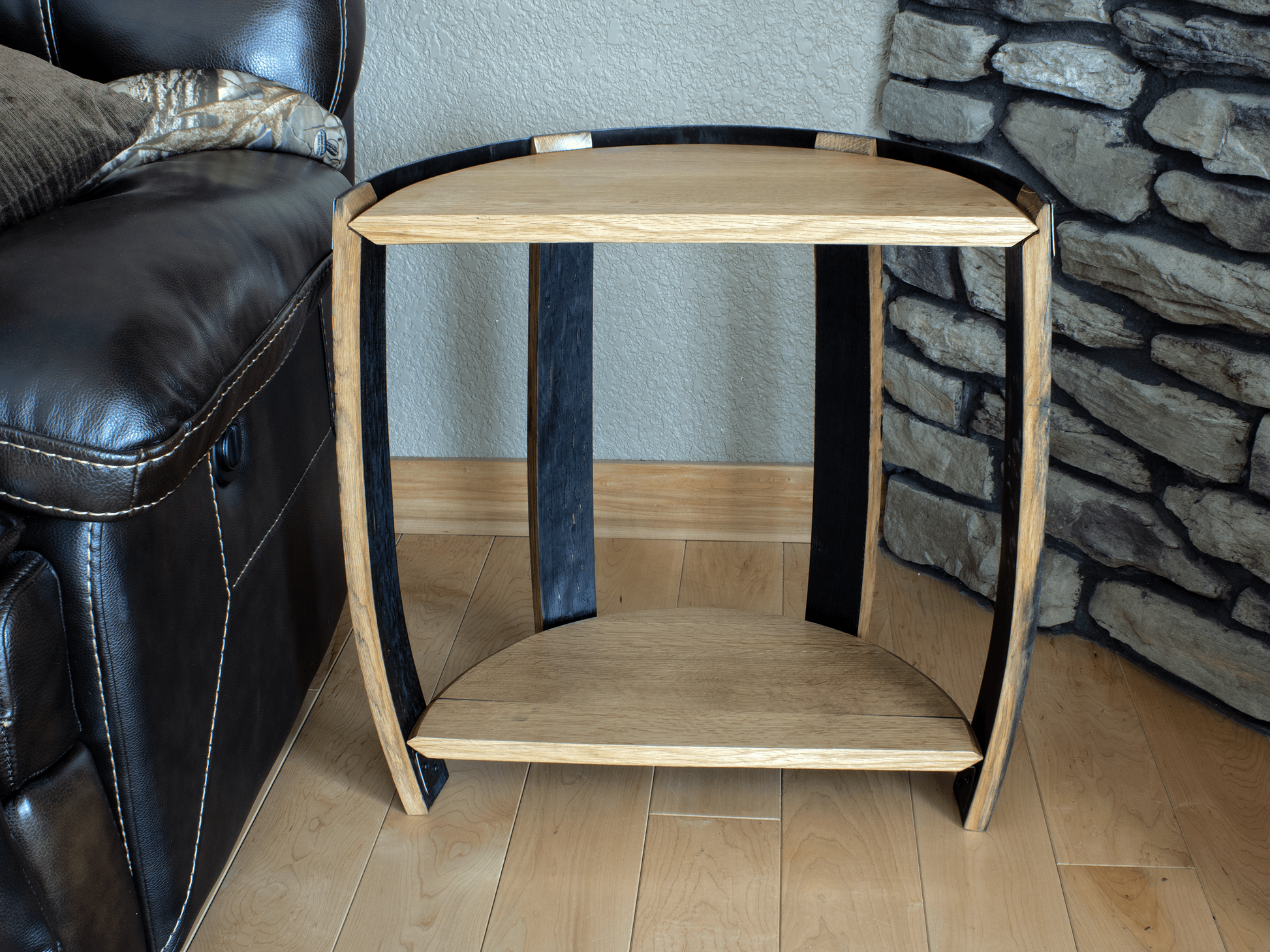 Distinctive back view of a half whiskey barrel end table, highlighting the deep charred texture on the inner side of the staves and the sturdy shelf design, set against a backdrop of stone and wood textures for a complete rustic look.