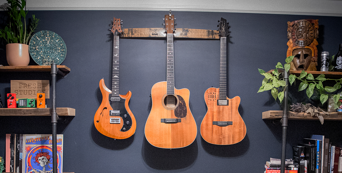 Three guitars displayed on a natural whiskey barrel stave triple guitar hanger without barrel hoop accents in a music room