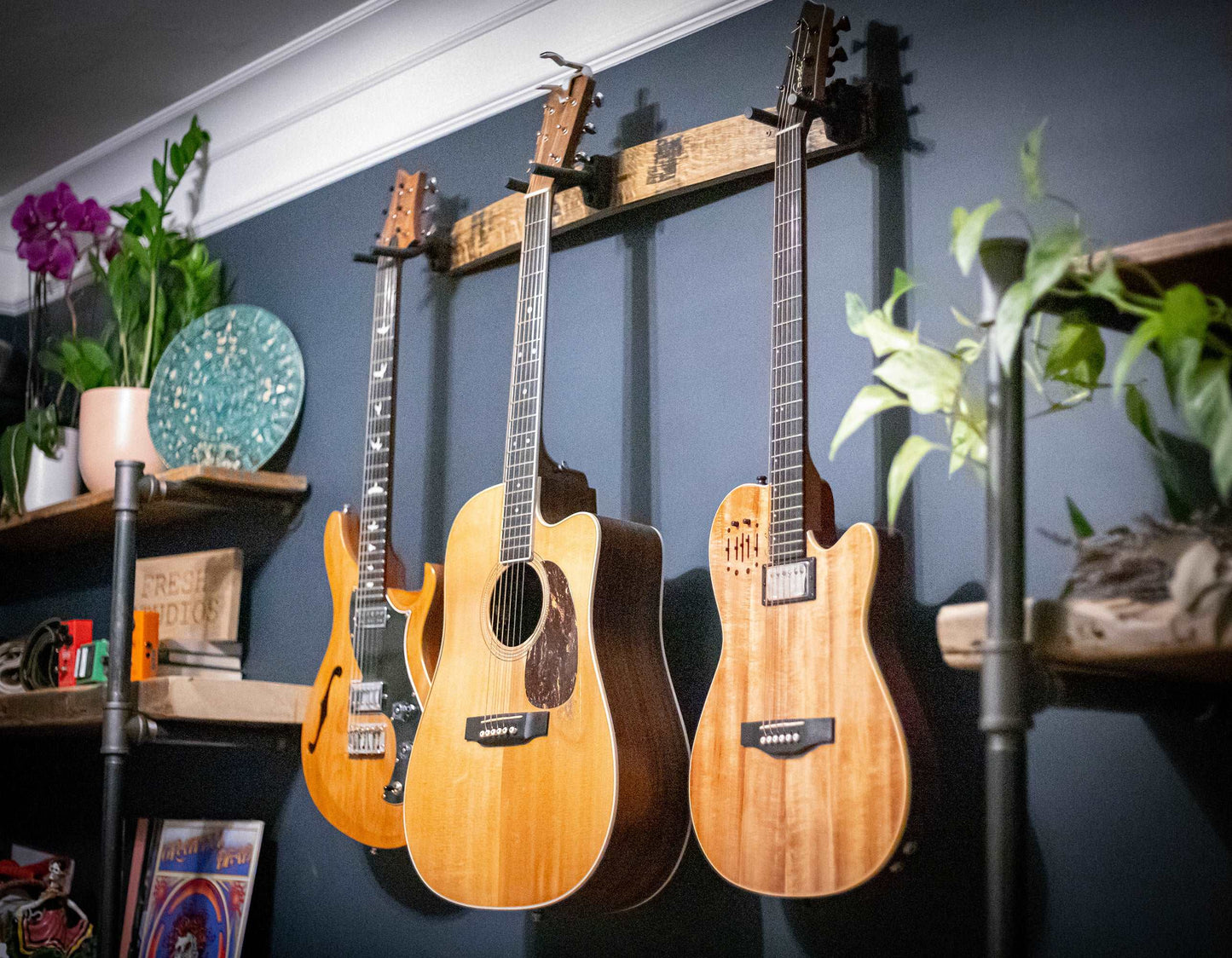     Close-up angled view of the 36-inch whiskey barrel stave guitar hanger, cradling three guitars with its sturdy, rustic charm, against a navy blue wall adorned with vibrant home decor accents, enhancing the musical vibe of the space.