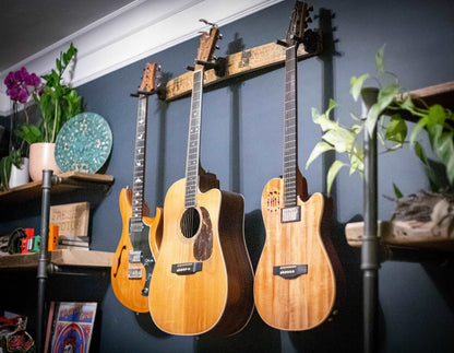     Close-up angled view of the 36-inch whiskey barrel stave guitar hanger, cradling three guitars with its sturdy, rustic charm, against a navy blue wall adorned with vibrant home decor accents, enhancing the musical vibe of the space.