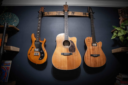 Frontal view from below of a 36-inch whiskey barrel stave guitar hanger, prominently displaying the unique wood grain and curvature, with three guitars mounted against a deep blue wall, enhancing the room's musical ambiance.